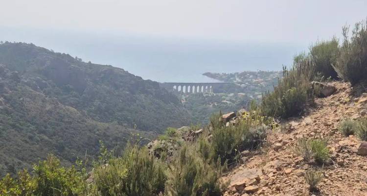 Hazy coastal landscape with green hills, a stone railway viaduct, and the Mediterranean Sea in the distance
