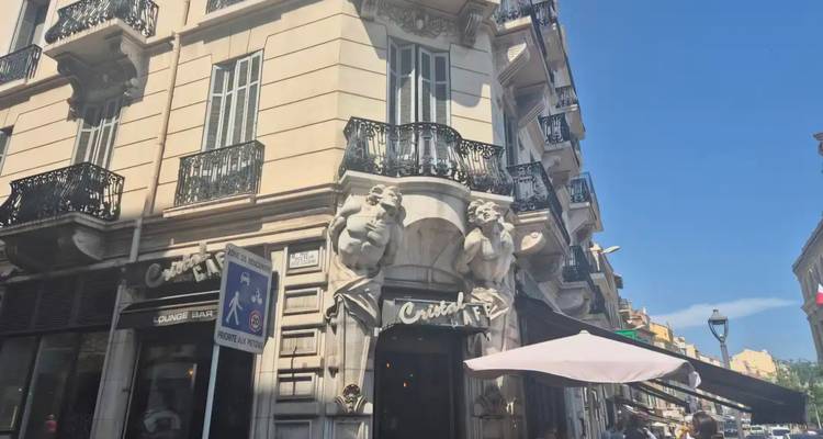 Street-level view of an elegant French corner building with ornate balconies and pedestrians below on a sunny day