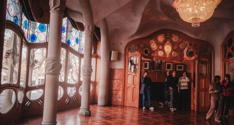 Habitación espaciosa dentro de la Casa Batlló con ventanas de vitrales y visitantes explorando.