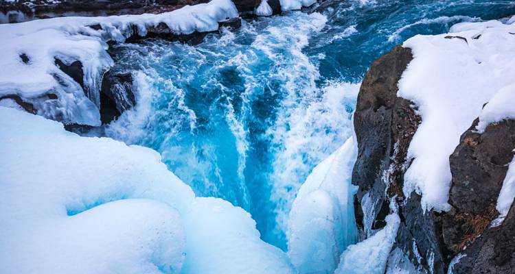 Gefrorener Wasserfall, der in eine enge vereiste Schlucht mit leuchtend blauem Wasser stürzt.