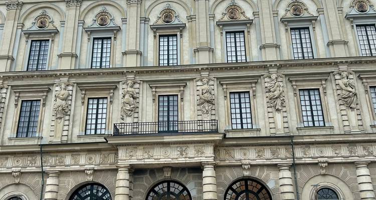 Fachada de piedra simétrica de un palacio con figuras esculpidas y filas de ventanas cuadradas.