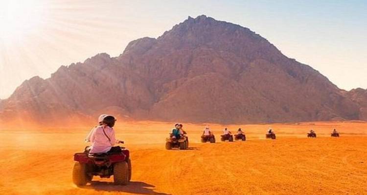 Los aventureros conducen quads a través de una llanura desértica naranja hacia una montaña rocosa