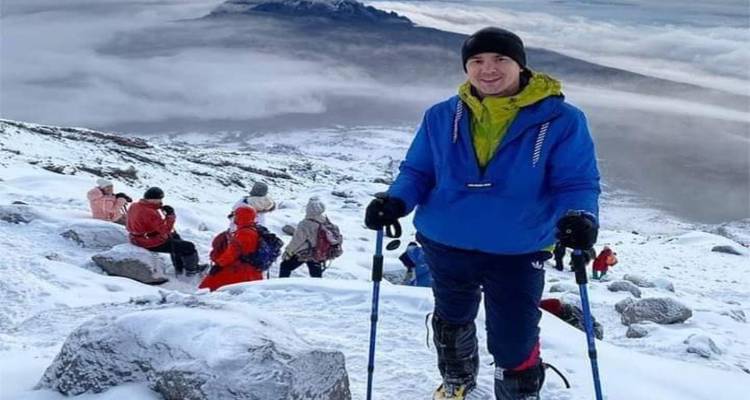 Hikers trek down a snow-covered volcanic slope with clouds blanketing the valley below.