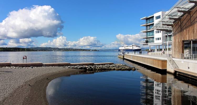 Front de mer moderne à Oslo avec des bâtiments de musée élégants, un traversier amarré et des nuages spectaculaires se reflétant dans une eau calme