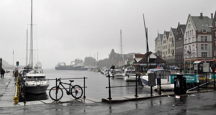 Scène portuaire pluvieuse avec des bateaux amarrés et les maisons en bois de Bryggen s'estompant dans la brume.