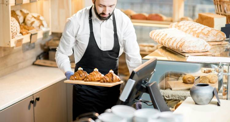 Bakery worker in apron presents a tray of fresh croissants