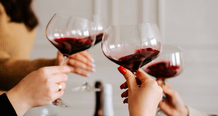 Multiple hands toasting with red wine in elegant stem glasses indoors.