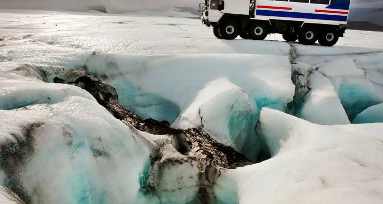 Specialized off-road vehicle crossing a crevassed blue glacier under overcast sky.