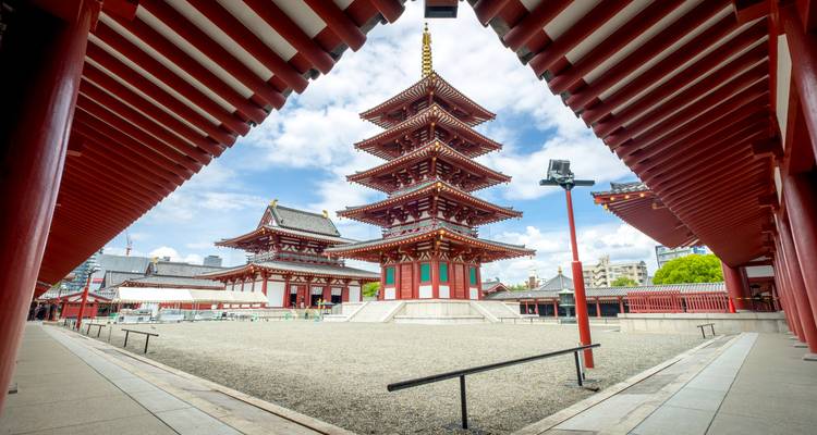Five-story red pagoda stands in a wide courtyard, framed symmetrically by temple eaves against a bright sky.