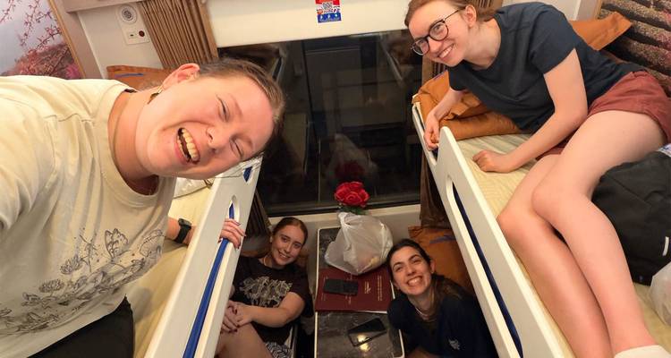 Smiling friends relaxing in sleeper train berths taking a selfie together.