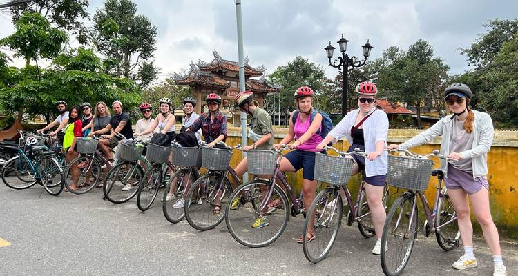 Cycling group lined up with helmets and rental bikes beside a historic yellow wall.