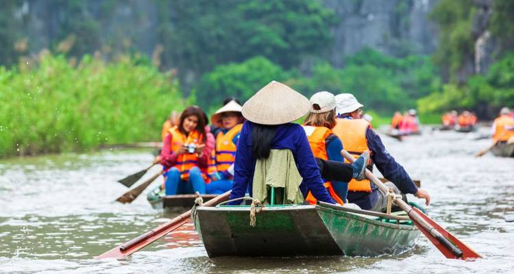 Les touristes, vêtus de gilets de sauvetage, sont transportés en barque à travers une gorge fluviale luxuriante dans de petits bateaux en bois.