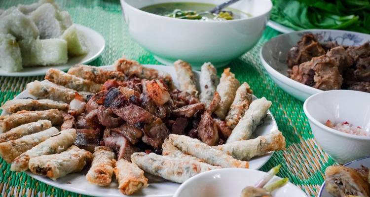 Gros plan d'un festin vietnamien présentant du porc grillé, des rouleaux de printemps frits et des sauces pour tremper sur un tapis vert.
