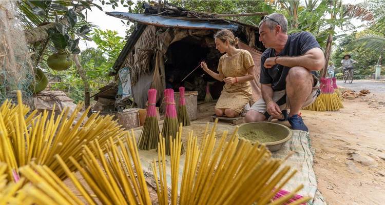 Les voyageurs s'accroupissent à côté de paquets de bâtons d'encens colorés tout en essayant des techniques artisanales traditionnelles dans une cabane rurale.