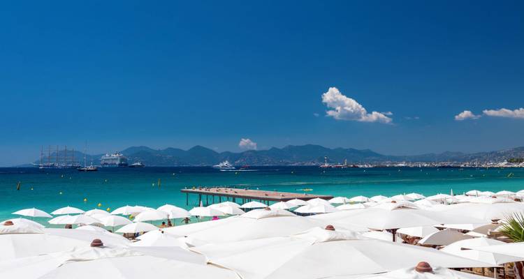 Des rangées de parasols blancs donnent sur les eaux turquoise de la Méditerranée et une jetée en bois.