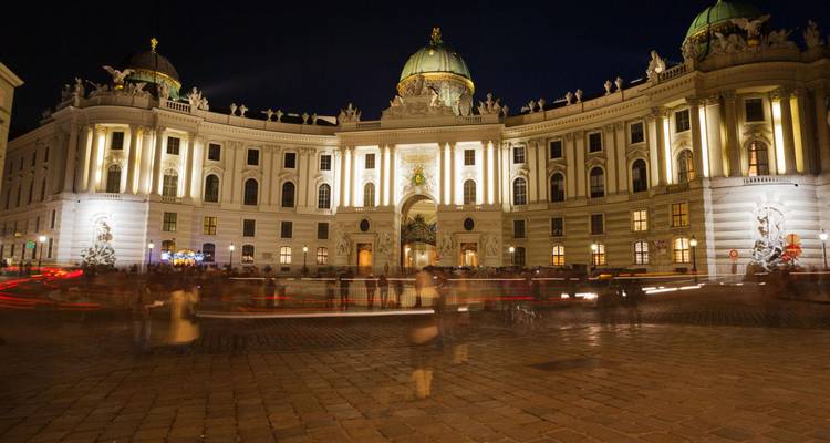 Nachtscène van Wenen's verlichte Hofburg Palace met bewegingsonscherpe menigte op het plein.
