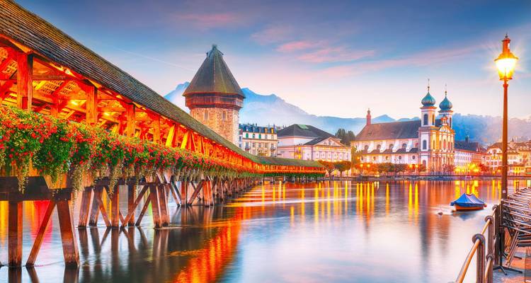De avondlichten weerspiegelen zich in de Reuß rivier onder de Kapelbrug en de Jezuïetenkerk van Luzern.