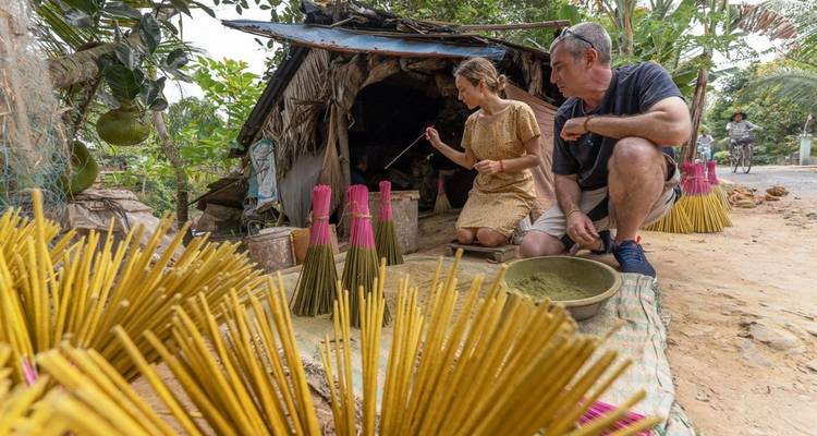 Les voyageurs s'accroupissent pour teindre des fagots brillants de bâtons d'encens à l'extérieur d'une cabane rustique.