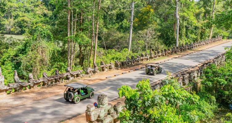 Deux jeeps vertes décapotables traversent un ancien pont de pierre à travers une jungle dense.