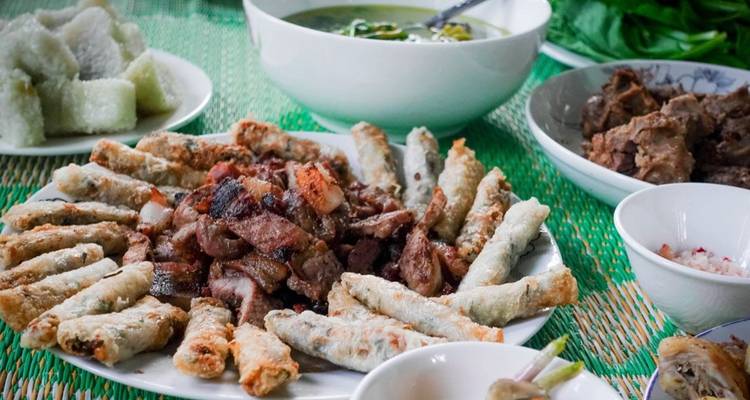 Un plateau de nems vietnamiens et de porc grillé disposés sur un tapis tissé vert.