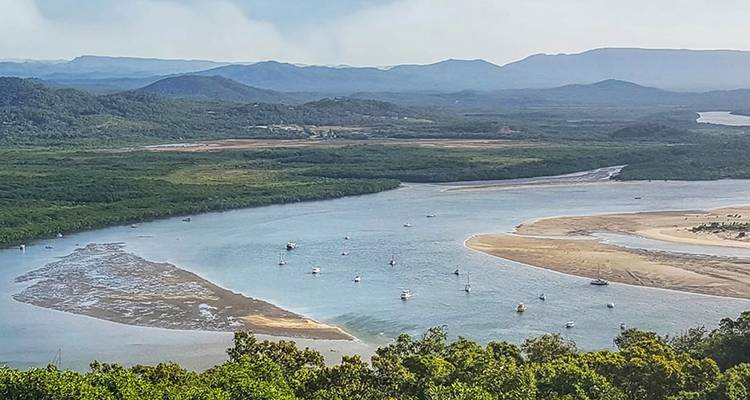 Point de vue élevé surplombant un delta fluvial côtier sinueux avec des bateaux ancrés et des chaînes de montagnes bleues au loin.