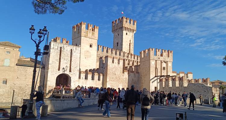 Las multitudes se reúnen afuera del impresionante Castillo Scaliger en Sirmione bajo un cielo azul brillante