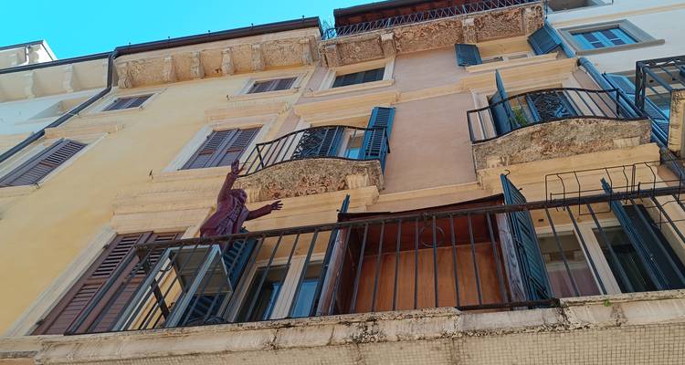 Ángulo ascendente de un edificio residencial italiano con persianas verdes y una estatua de balcón peculiar