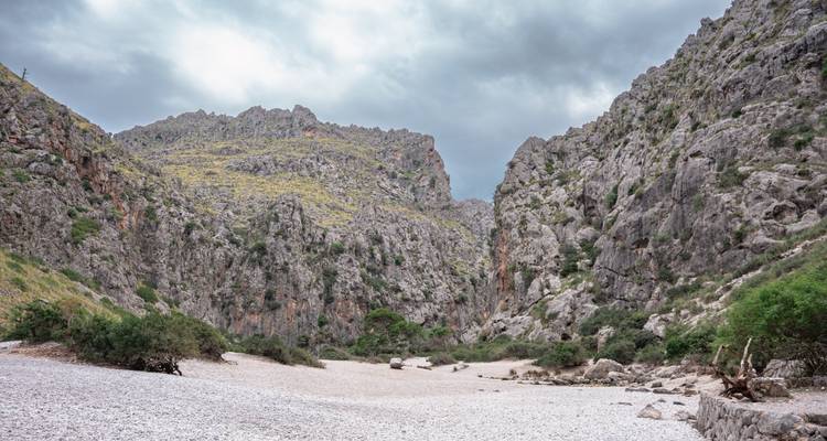 Lit de rivière rocailleux et aride entre des parois de canyon escarpées et accidentées sous un ciel gris