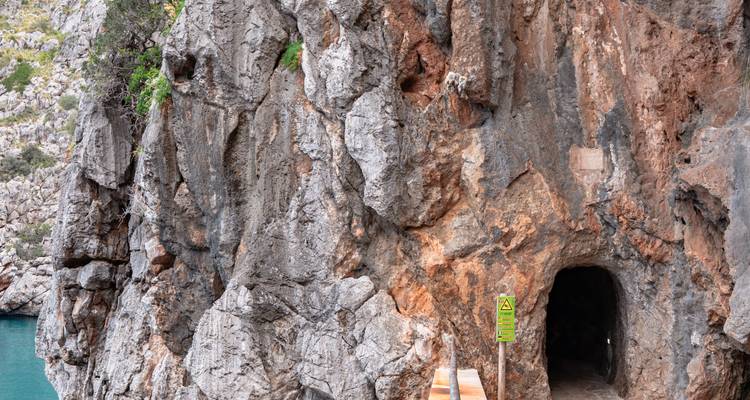 Entrée du tunnel creusée dans la paroi rocheuse abrupte bordant l'eau turquoise