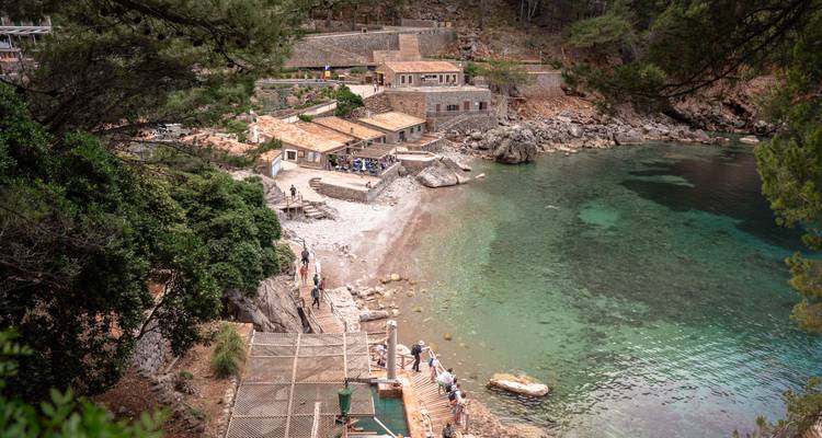 Anse isolée aux eaux cristallines, maisons en pierre rustiques et visiteurs sur une terrasse en bois