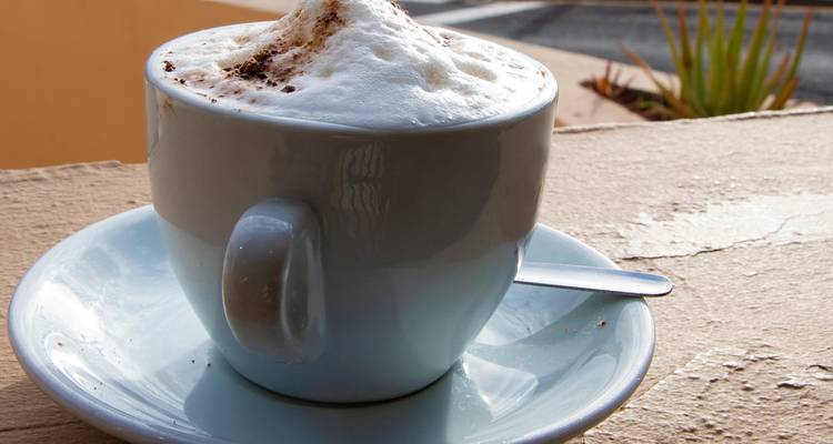 Gros plan d'un cappuccino mousseux dans une tasse et une soucoupe bleu pâle