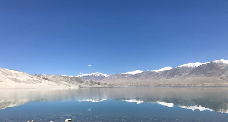 Crystal clear mountain lake reflecting snow-capped peaks beneath a deep blue sky.