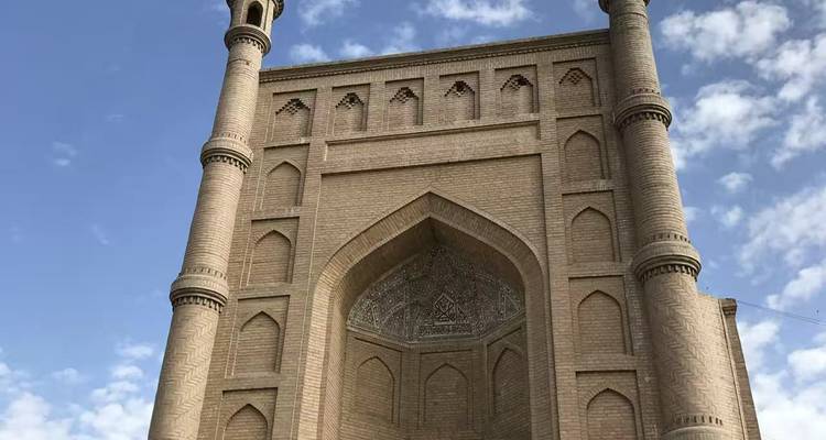 Tall brick Islamic gate with twin minarets against a partly cloudy sky.