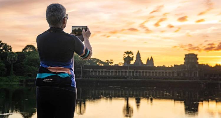 Un voyageur photographiant la silhouette d'Angkor Wat à travers une douve réfléchissante à l'aube.