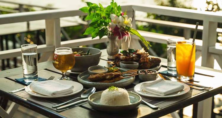 Table dressée accueillante garnie de brochettes grillées, de riz, de bière et de jus de fruits sur une terrasse donnant sur la verdure.
