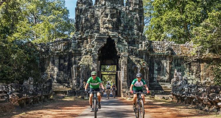 Des cyclistes traversant la porte en pierre monumentale d'Angkor Thom entourée d'une jungle luxuriante.