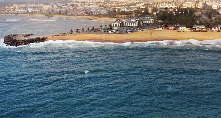 Luftaufnahme einer Küstenstadt in Namibia, langer Sandstrand und rollende Atlantikwellen.