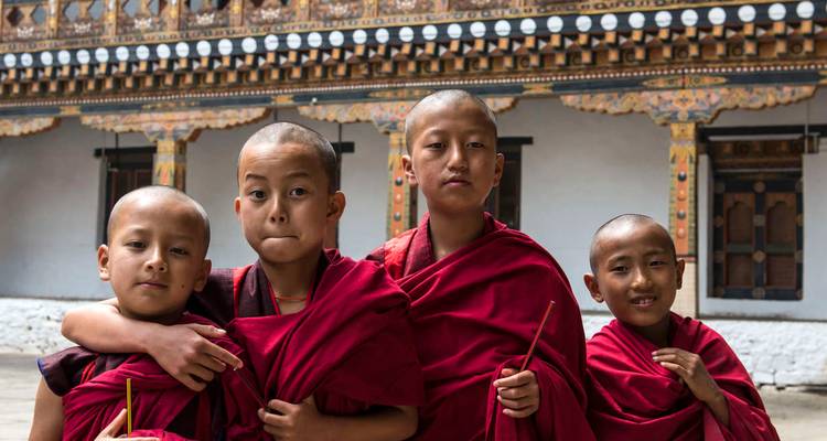 Groupe de jeunes moines novices bouddhistes en robes rouges posant dans une cour de monastère.