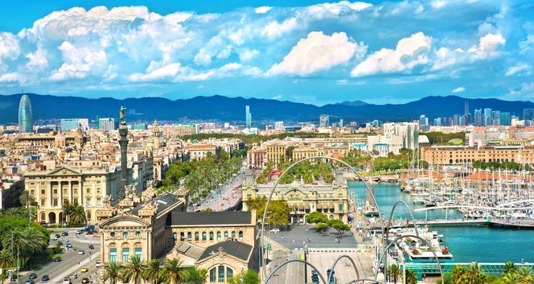 Panoramablick über Barcelonas historisches Zentrum, Hafen und Bergkulisse unter hellem Wolkenhimmel.