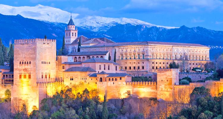 Avondaanzicht van het verlichte Alhambrapaleizencomplex met sneeuwbedekte bergen erachter.