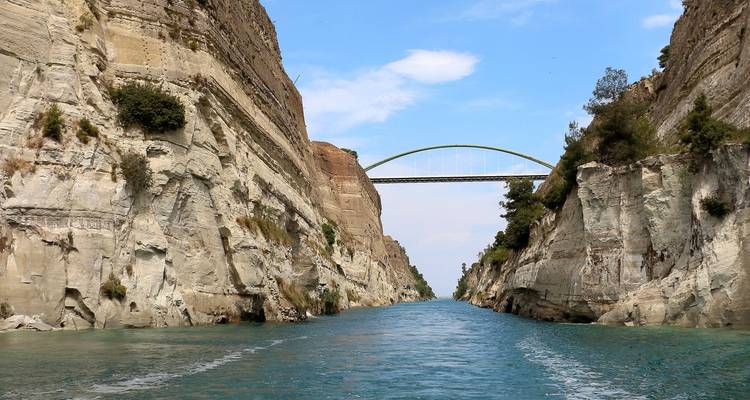 Narrow blue waters of Corinth Canal flanked by sheer limestone walls with an arched bridge overhead