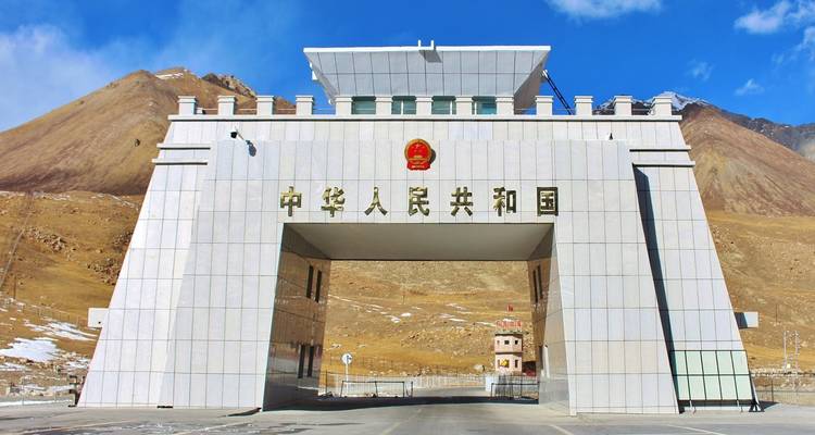 Weißes Marmortor am Khunjerab-Pass an der Grenze zwischen Pakistan und China mit kahlen Bergen im Hintergrund.
