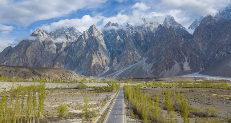 Weitreichender Blick auf die zerklüfteten Passu-Kegel und die Karakoram-Straße, gesäumt von Pappelbäumen.