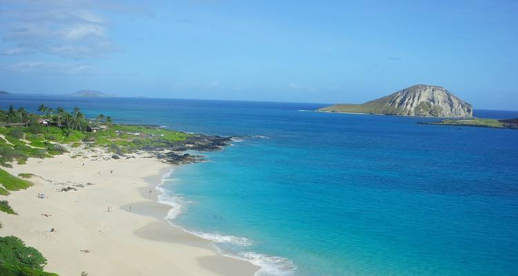 Wide sandy beach with turquoise water and an offshore islet under a bright blue sky.