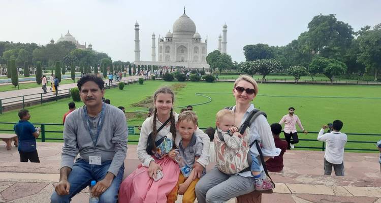 Family with young children posing in front of the Taj Mahal across the gardens on a cloudy day.