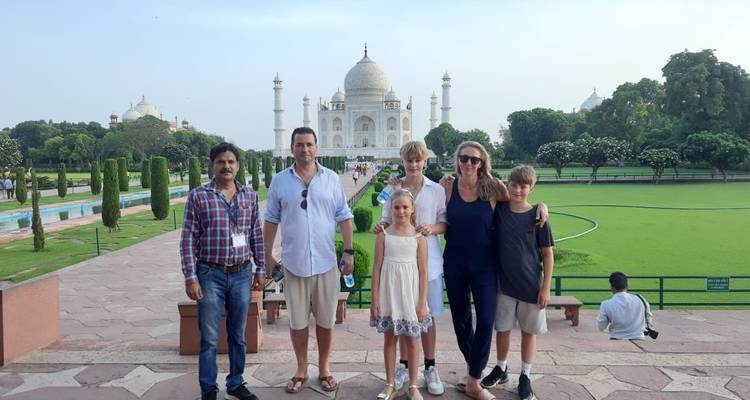 Family and guide posing for a photo with the Taj Mahal and manicured gardens behind them.