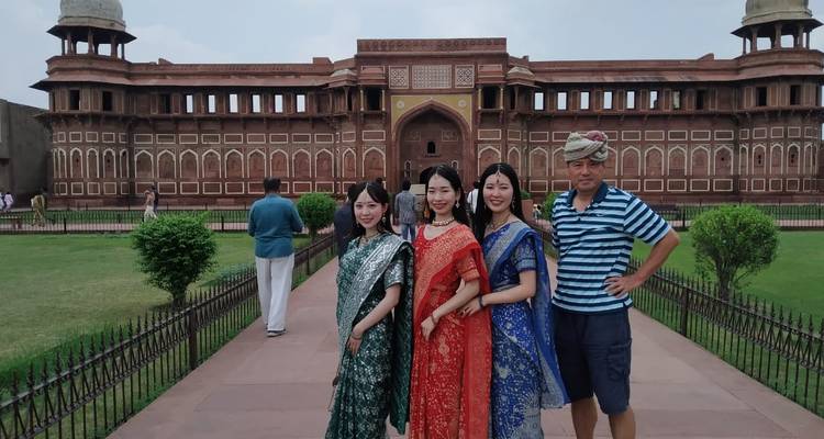 Tourists dressed in colorful saris posing in front of the ornate red sandstone walls of Agra Fort.