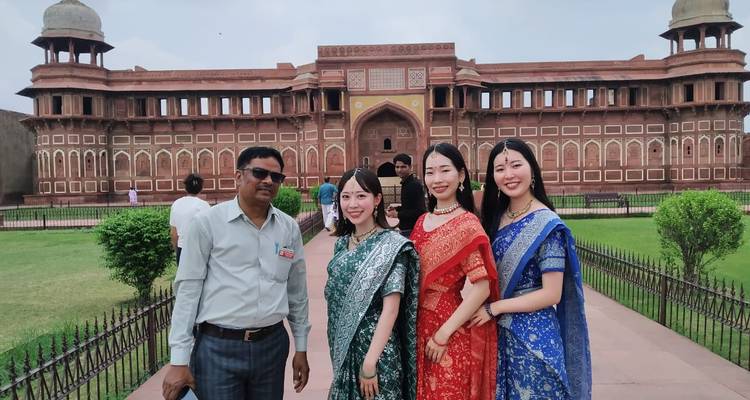 Guide and visitors in traditional attire smiling in front of Agra Fort’s main gate.