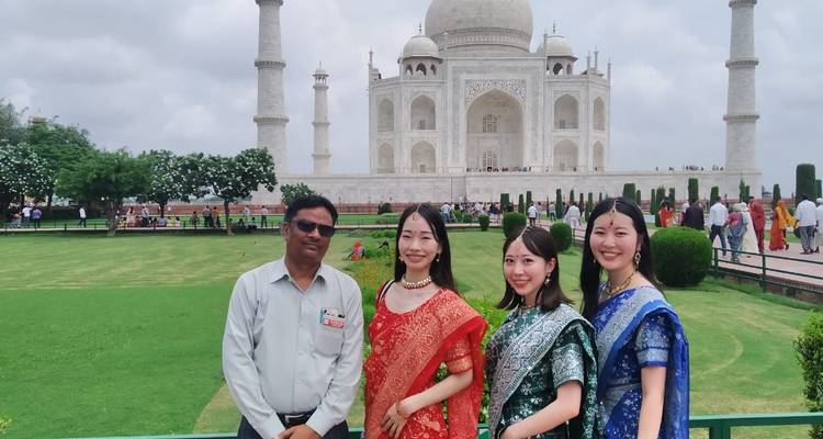 Small group wearing saris and guide posing on the Taj Mahal lawns with the white marble mausoleum behind.