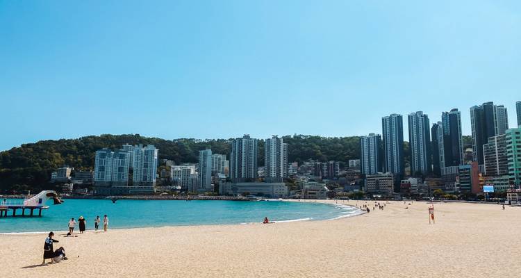 Une large plage de sable fin rencontre des eaux turquoise avec une skyline moderne de gratte-ciel au-delà.
